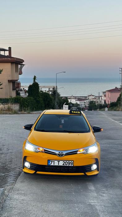 Yenişehir Taksi sarı taksi aracı, deniz manzaralı yol üzerinde